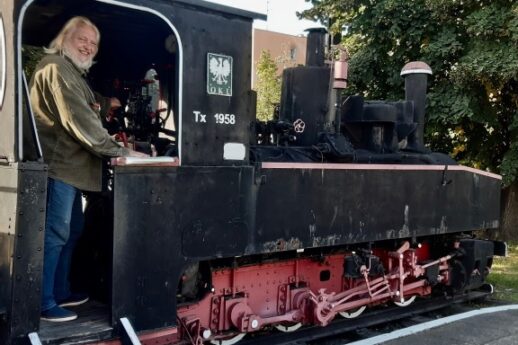 Osoba stoi w otwartym wejściu do kabiny ciemnej lokomotywy parowej oznaczonej cyframi 