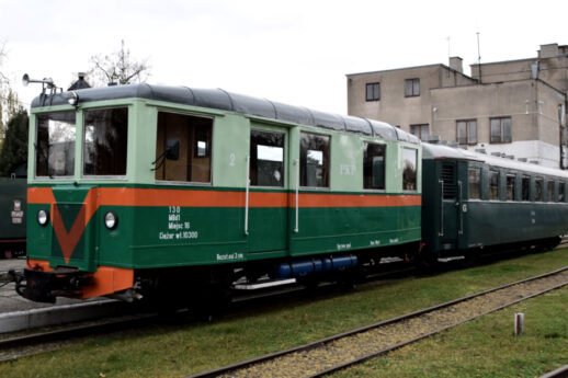Stoi zielono-pomarańczowy wąskotorowy wagon pasażerski z napisem 