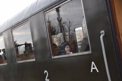 Dziecko wygląda przez okno zielonego wagonu kolejowego oznaczonego numerem 