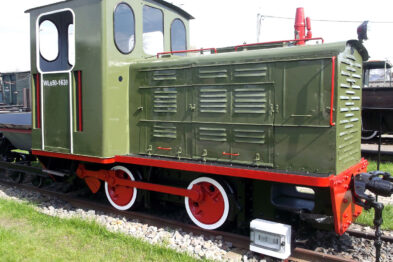 Lokomotywa spalinowa o zielono-czerwonej kolorystyce stoi na torach kolejowych. Posiada białe obramowanie okien, a jej koła i zderzaki są pomalowane na czerwono. Na bocznej ścianie kabiny widnieje numer 