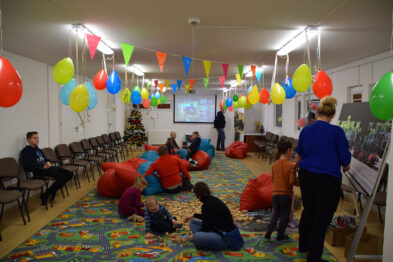 Sala udekorowana balonami. Na dywanie dzieci i dorośli układają drewniane klocki