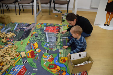 Sala udekorowana balonami. Na dywanie dzieci i dorośli układają wielkoformatowe puzzle.
