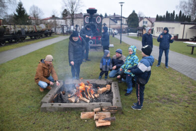 Grupa dorosłych i dzieci piecze kiełbaski przy ognisku