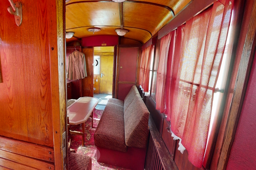 Wnętrze wagonu. Beżowa kanapa i stolik, w oknach czerwone zasłonki