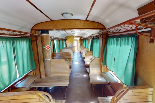 Wnętrze wagonu kolejowego z drewnianymi ławkami i zielonymi zasłonkami