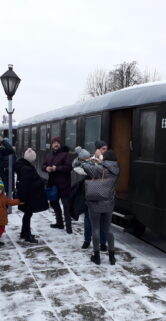 Grupa osób w skansenie muzeum. Widoczny wagon osobowy w tle.