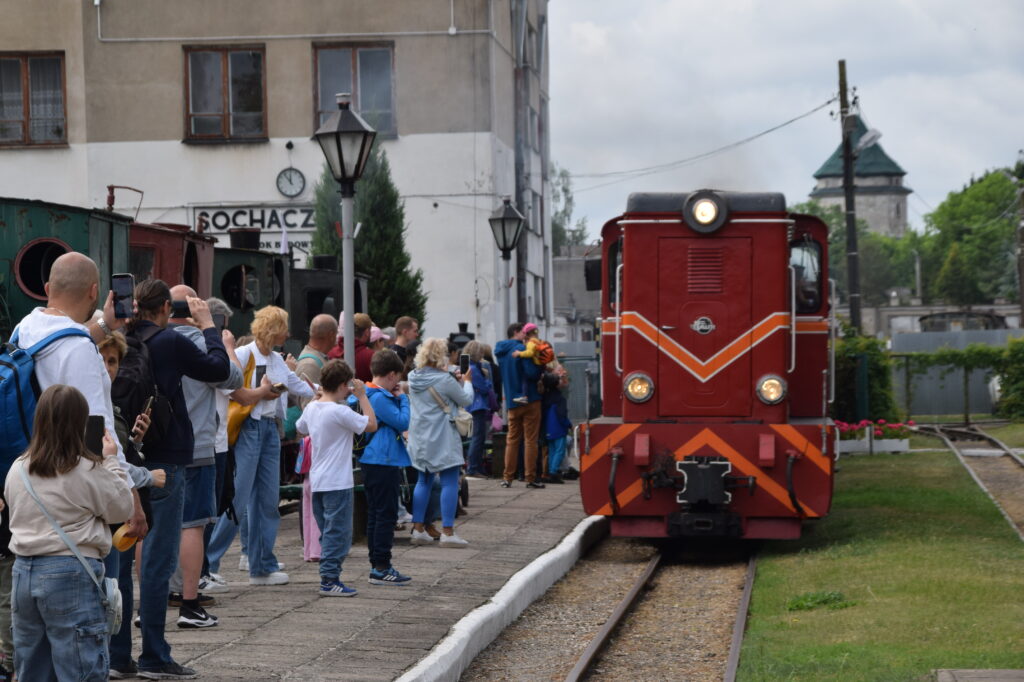 Muzealny pociąg z czerwona lokomotywą wjeżdża w peron, na którym stoją turyści